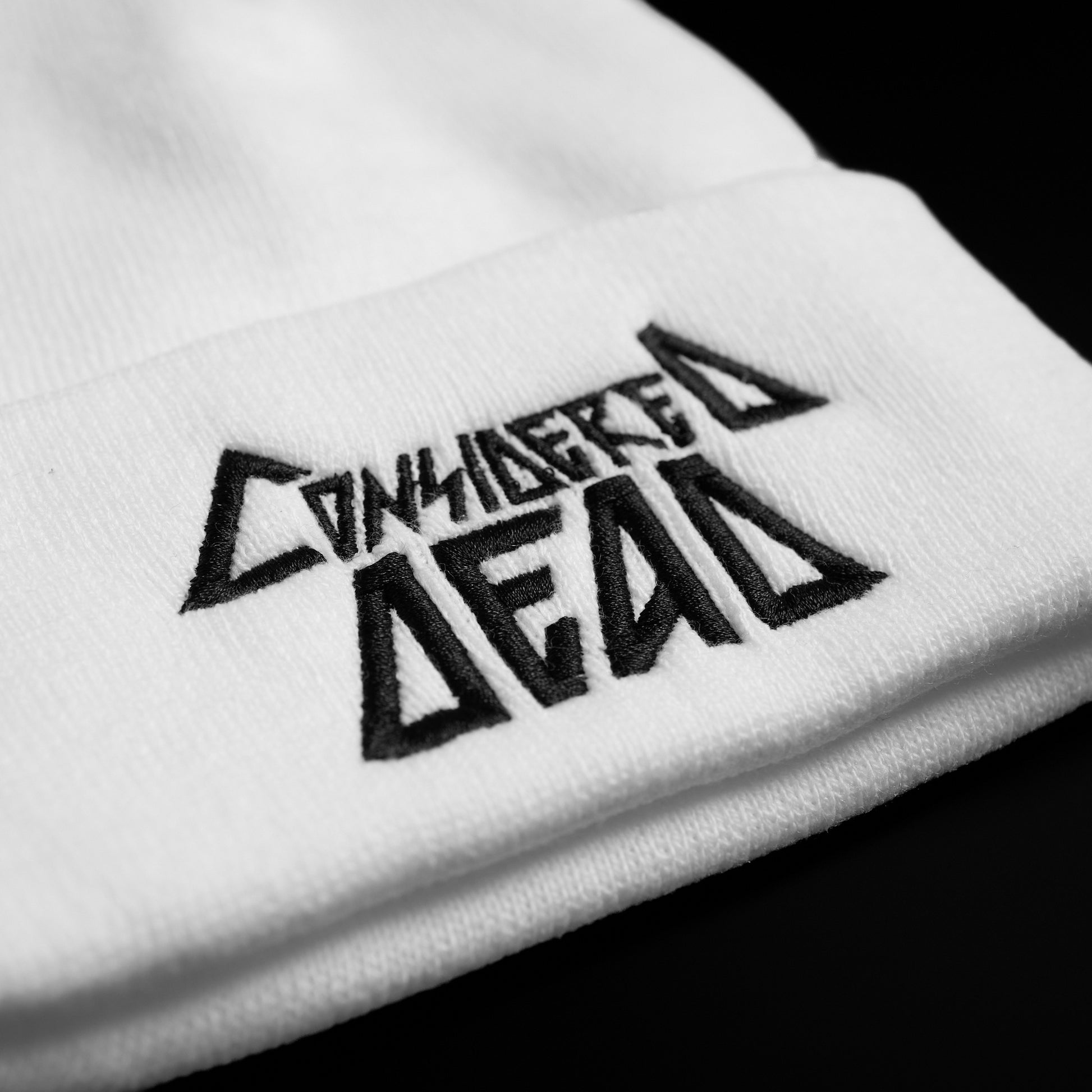 A white knit beanie with the 'Considered Dead' logo embroidered in black on the cuff.